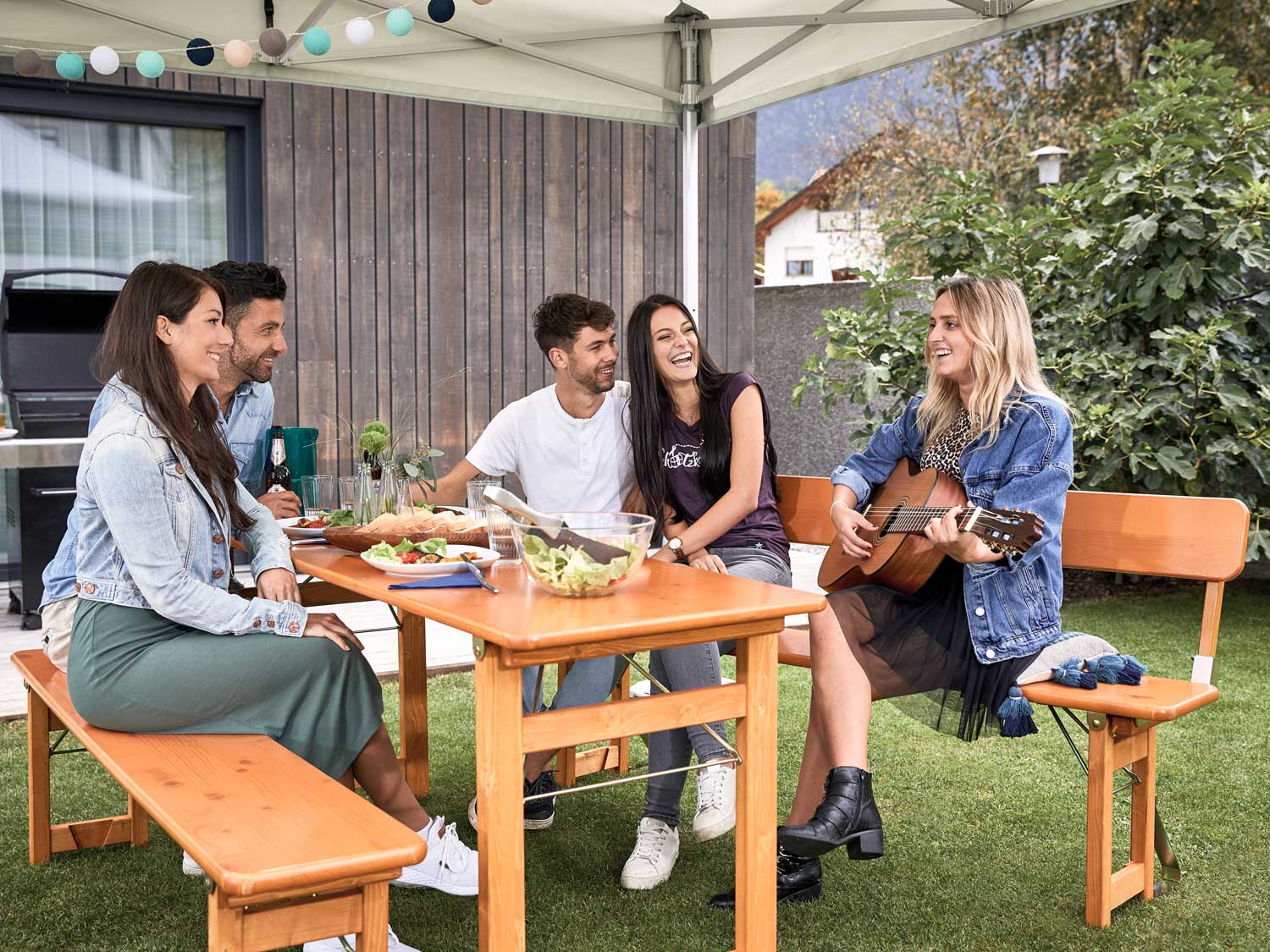 Quattro persone si godono la musica suonata da una donna con la chitarra e si siedono sul set Rustica nel giardino.
