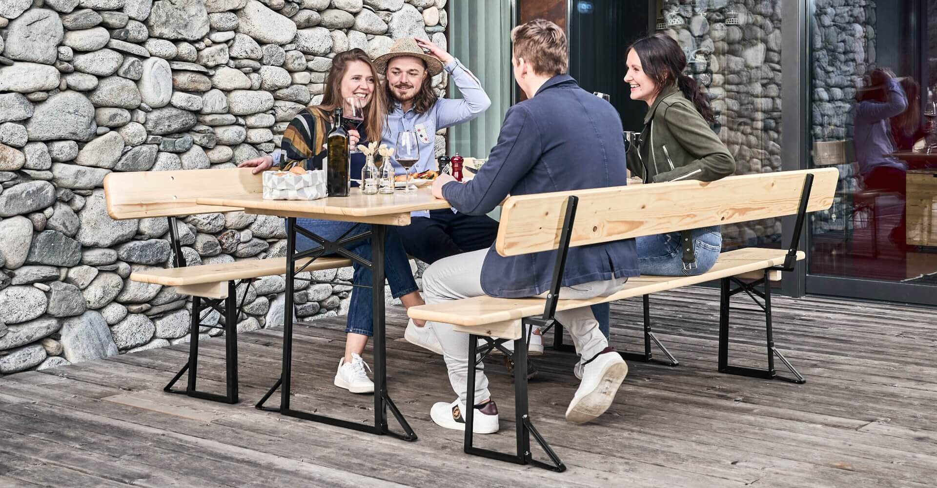 Vier Personen essen zu Mittag auf einer Bierzeltgarnitur mit Lehne auf der Terrasse.