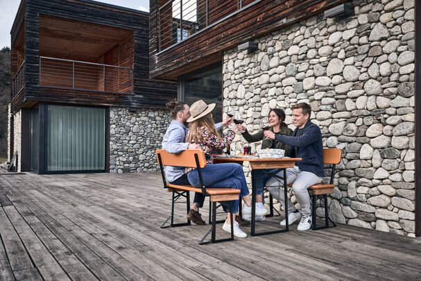 Four people have lunch on a small beer garden table set with backrest on the terrace.