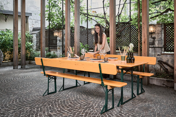 A woman decorates a wide beer garden table set with backrest in the outdoor area of the Vitis restaurant.