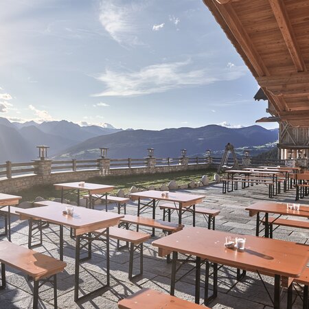 On a terrace of a cottage are small beer garden table sets in the sun.