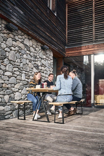 Vier Personen sitzen auf der Bierzeltgarnitur in Beinfreiheit in Natur auf einer Terrasse.