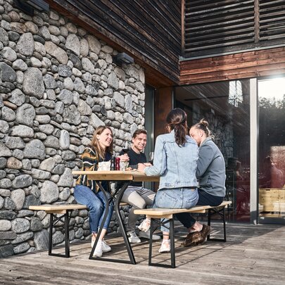 Four people sitting on the beer garden table set in legroom in nature on a terrace.