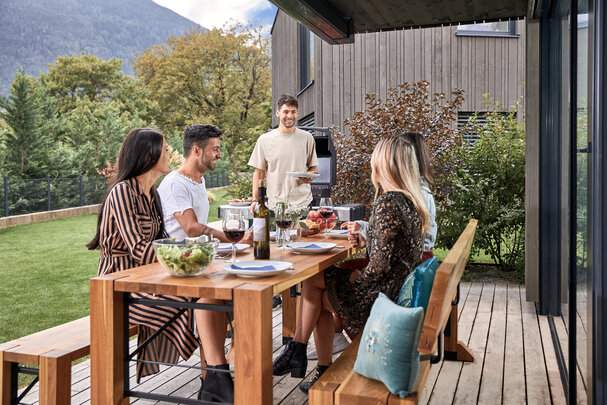 Es findet ein Grillen im Garten statt und 4 Personen sitzen bereits auf der Designgarnitur Lago.