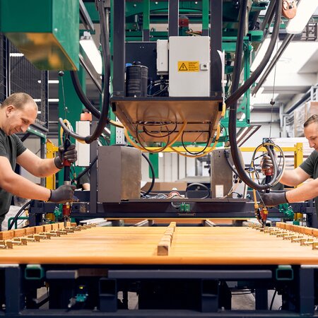 Two employees use a machine to assemble the locking mechanisms on several RUKU1952 beer benches.