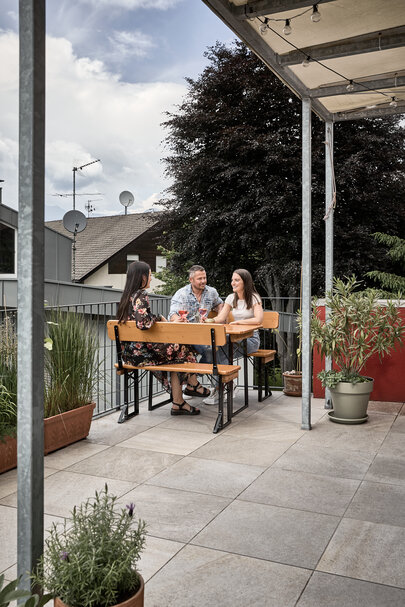 Three people sitting on the small beer garden table set Shorty with backrest on a balcony.