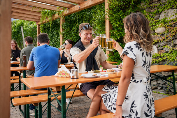 Mehrere Personen genießen auf den klassischen Bierzeltgarnituren Marende und Bier beim Guggerhof.