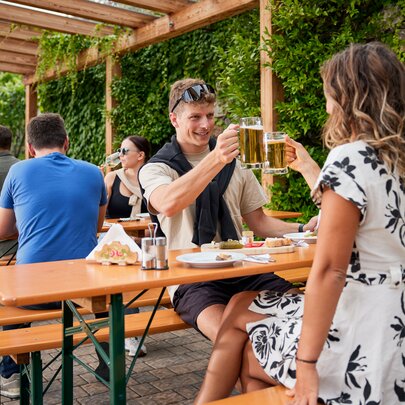 Mehrere Personen genießen auf den klassischen Bierzeltgarnituren Marende und Bier beim Guggerhof.