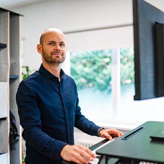 Employee at his desk An employee of the Zingerle Group is standing at his ergonomic standing desk.