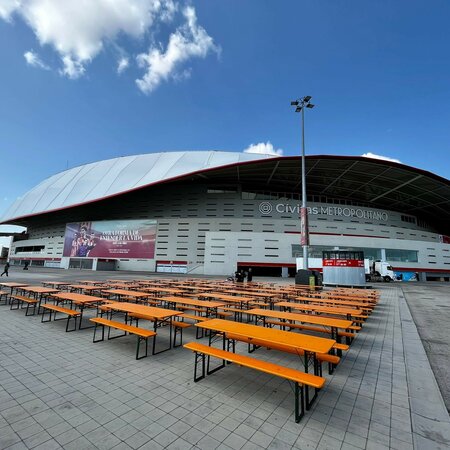 Classic beer garden table sets are set up in front of the Atletico de Madrid stadium.