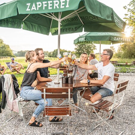 4 people are toasting with their beer on the beer garden furniture on the terrace of a pub.