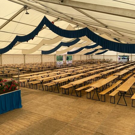 Beer garden table sets with legroom are placed in a marquee.