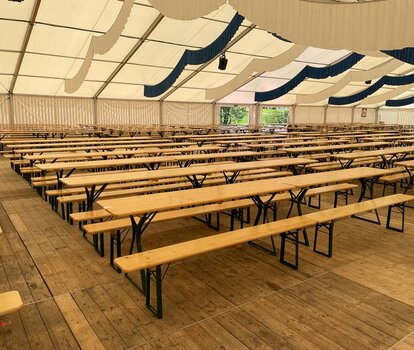 Mehrere Bierzeltgarnituren mit Beinfreiheit sind in einem Festzelt aufgestellt.