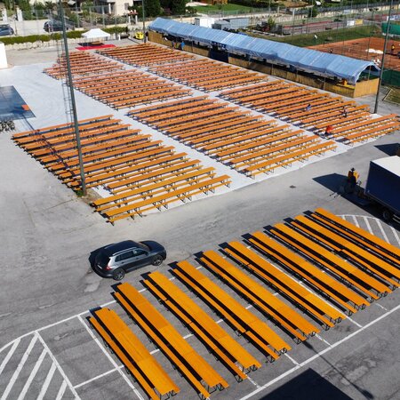 Su una grande area asfaltata accanto a un campo da tennis, sono stati disposti in più blocchi 350 set da birreria classici nel colore pino.